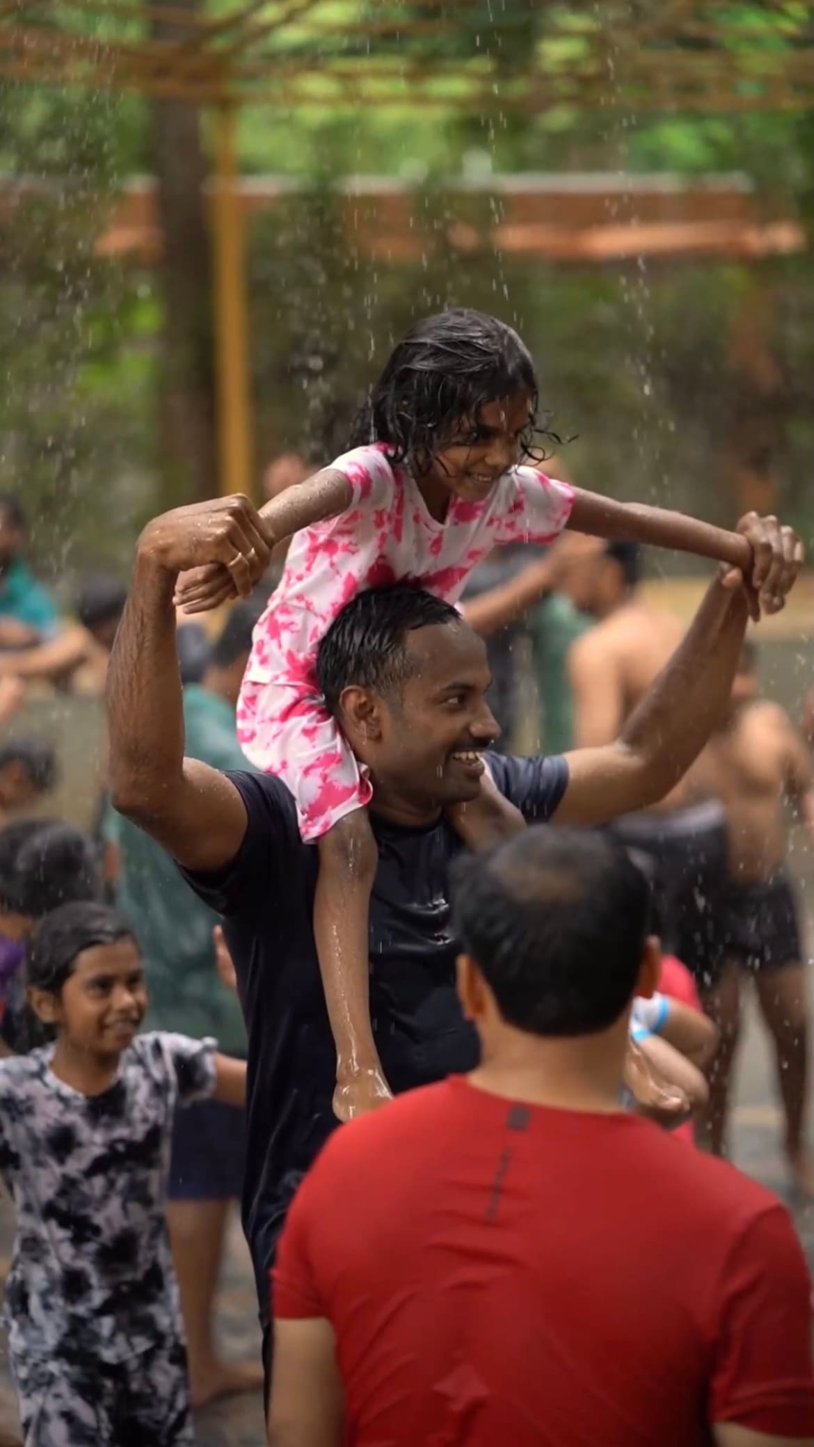 Father and daughter under the rain dance sprinklers, mid-celebration